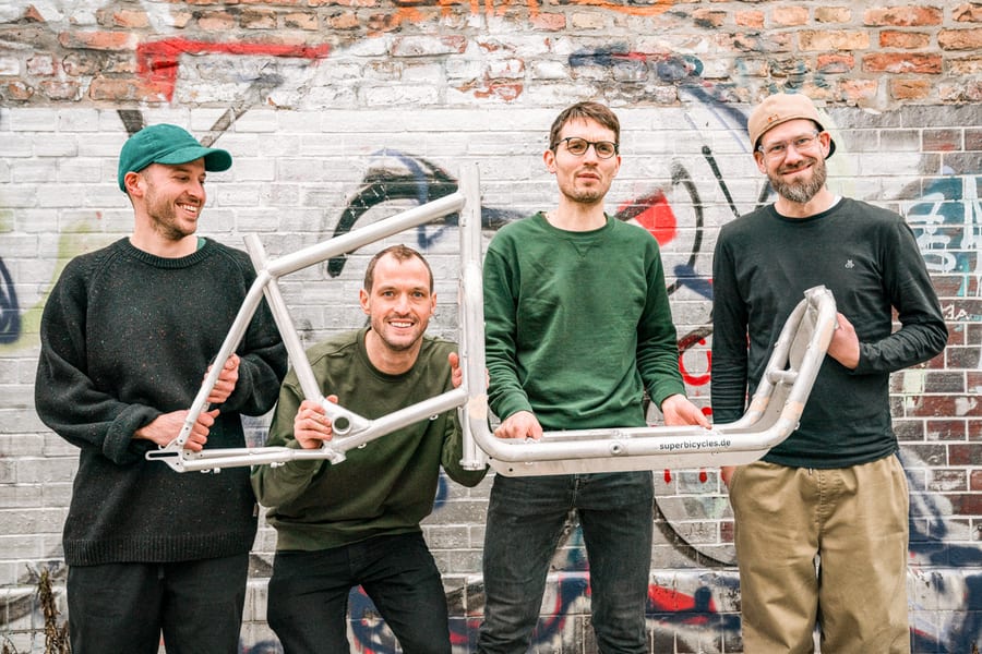 Die vier Gründer Max, Daniel, Moritz und Andi mit einem Rahmen vor einer Graffiti-Wand